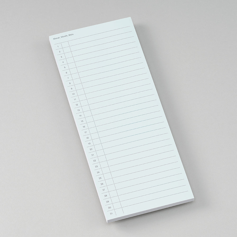 A single-page notepad with a monthly calendar grid layout, photographed on a neutral light gray background.