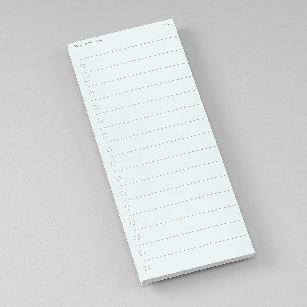 A white notepad with printed checklist lines and small header text, photographed on a clean light gray background.