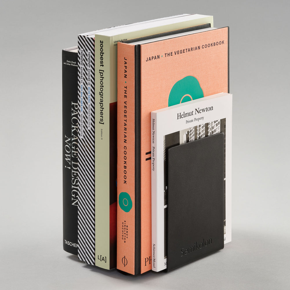 A vertical stack of books and a notebook on a light gray studio background. Visible titles include 'Packaged Design Vol.