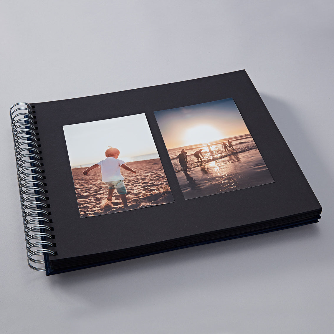 Black photo album with two images of a child on a beach.